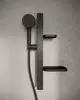 Brausekombination von Ideal Standard mit schwarzem Handbrausekopf und zwei Ablagen, montiert an einer hellen Wand aus Sichtbeton.